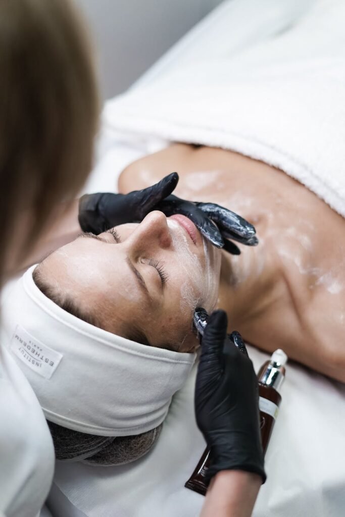 beautician removing clay cosmetic mask from woman face