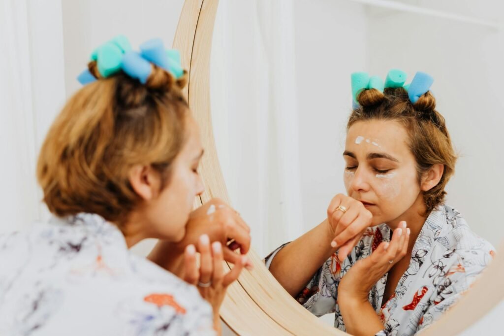 woman with curlers on hair smelling face cream on skin