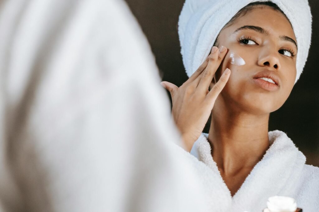 ethnic woman applying cream on face in morning
