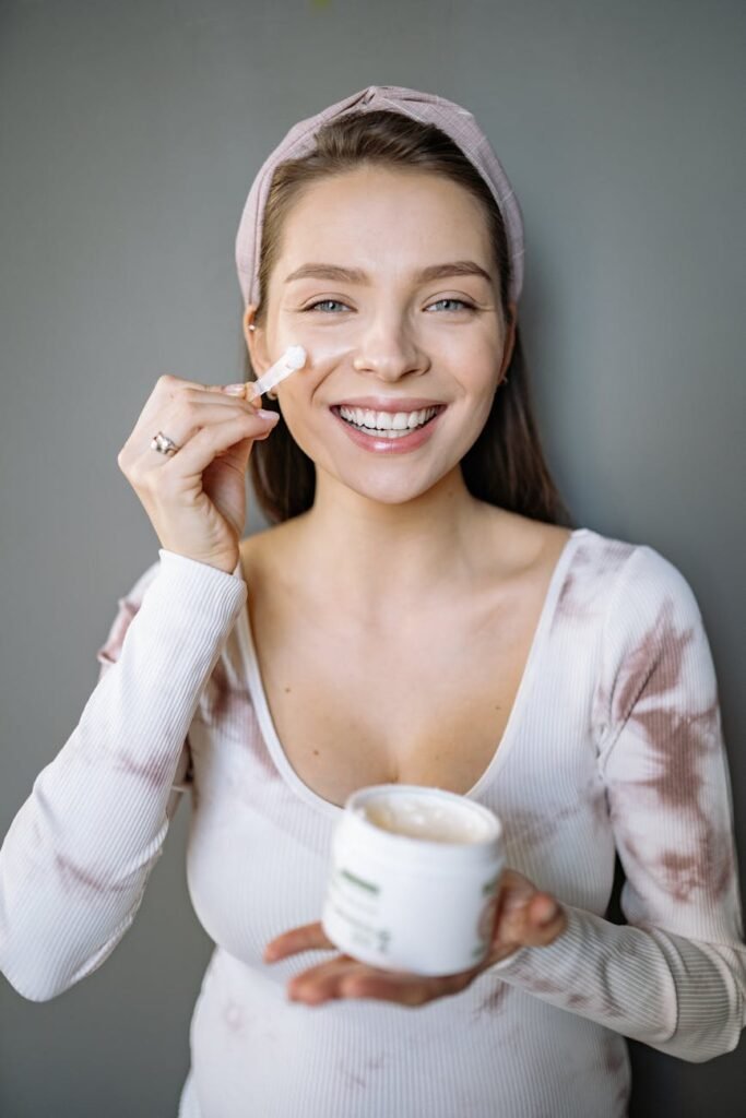 smiling woman putting cream on her face looking at camera